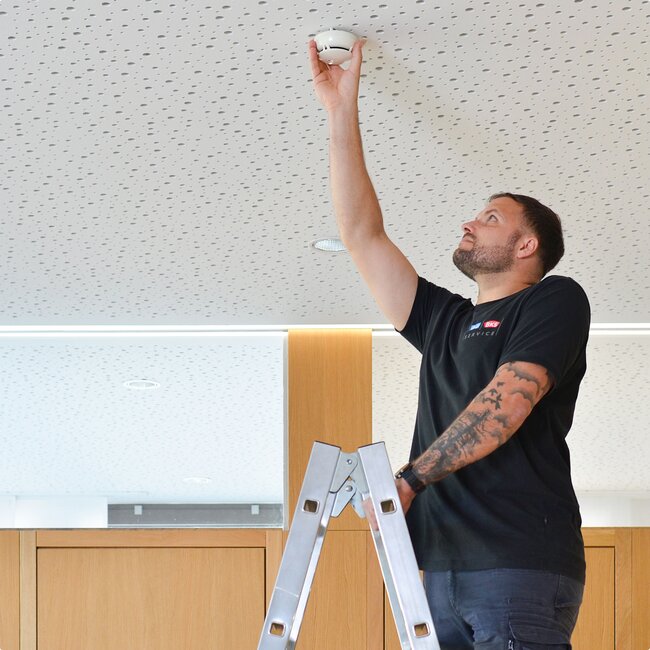 Techniker montiert Rauchmelder an Decke